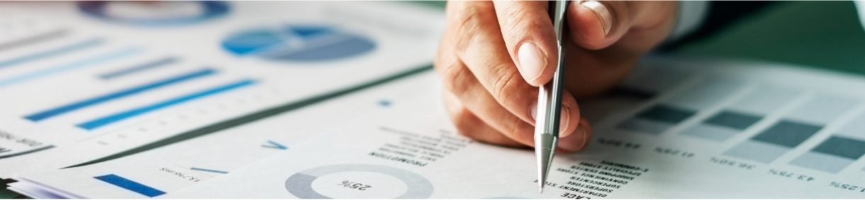 Hand holding a pen over financial charts and data