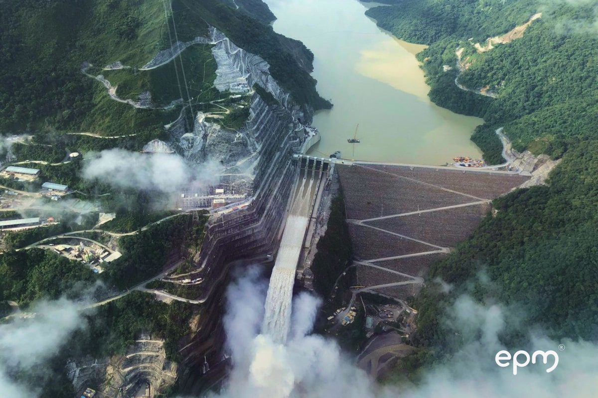 Photograph of a large hydroelectric dam surrounded by green mountains and a reservoir with murky waters.